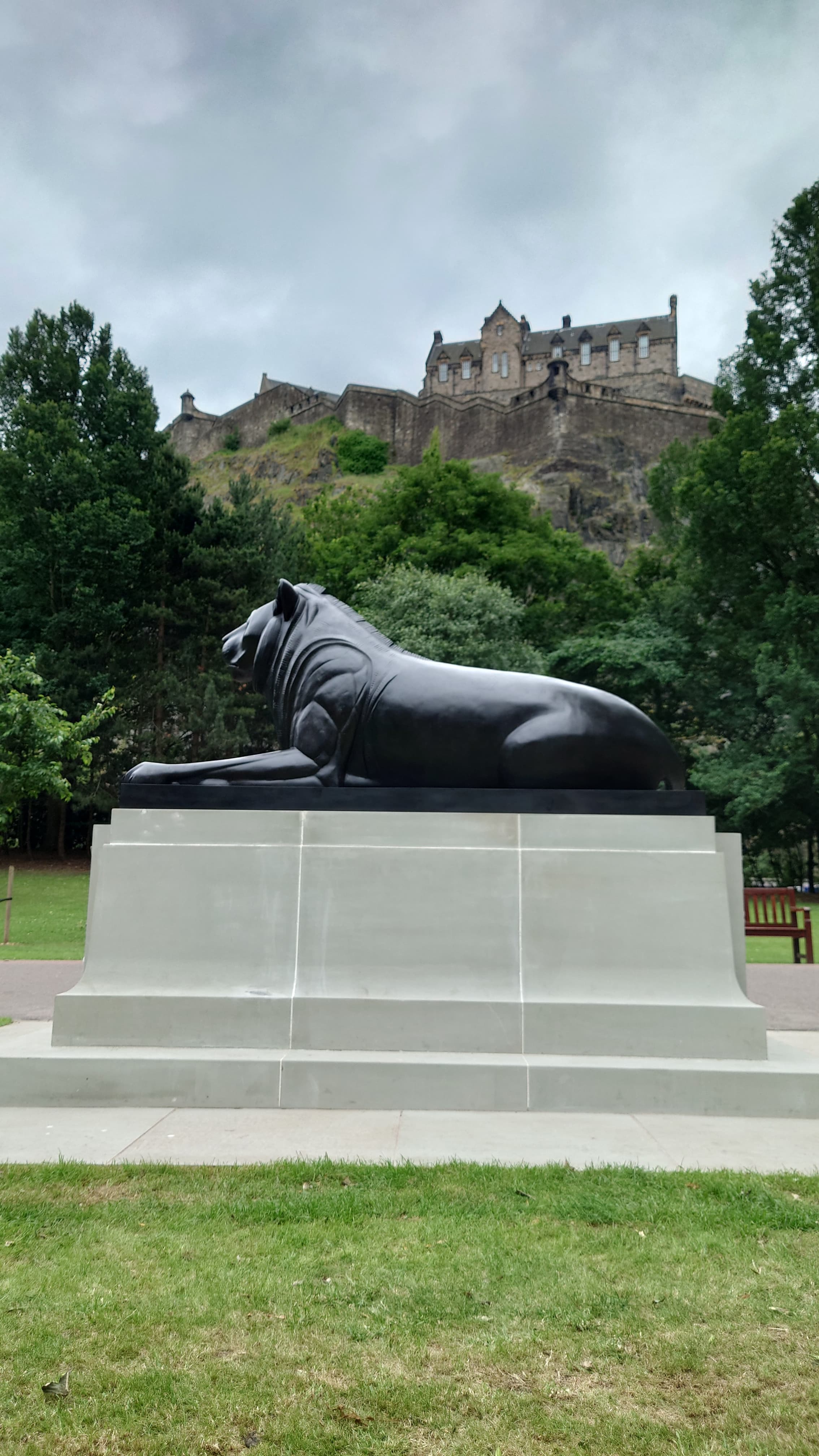 Lion statue in Princes Street Gardens with Edinburgh Castle rising above the trees.